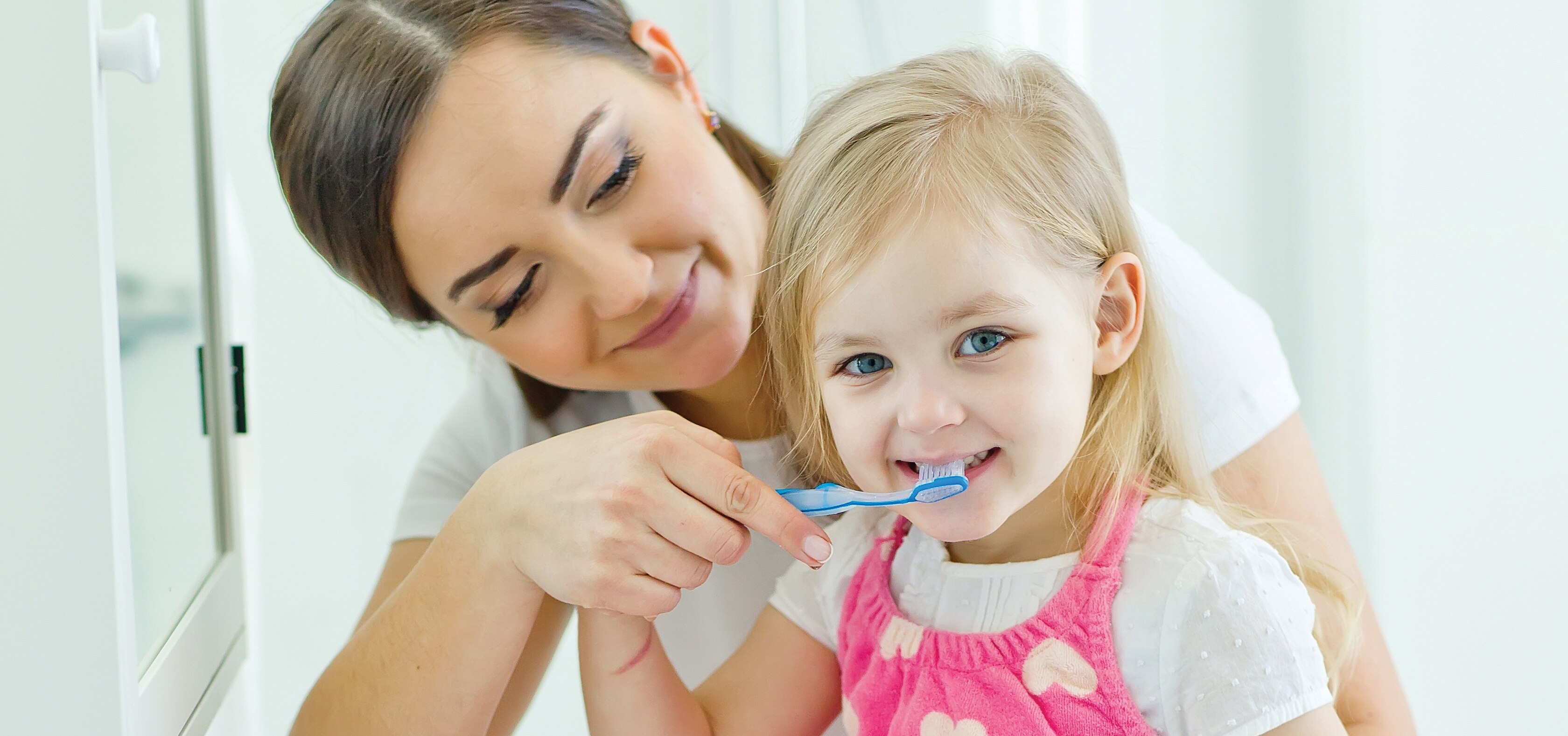 mother helping toddler brush her teeth