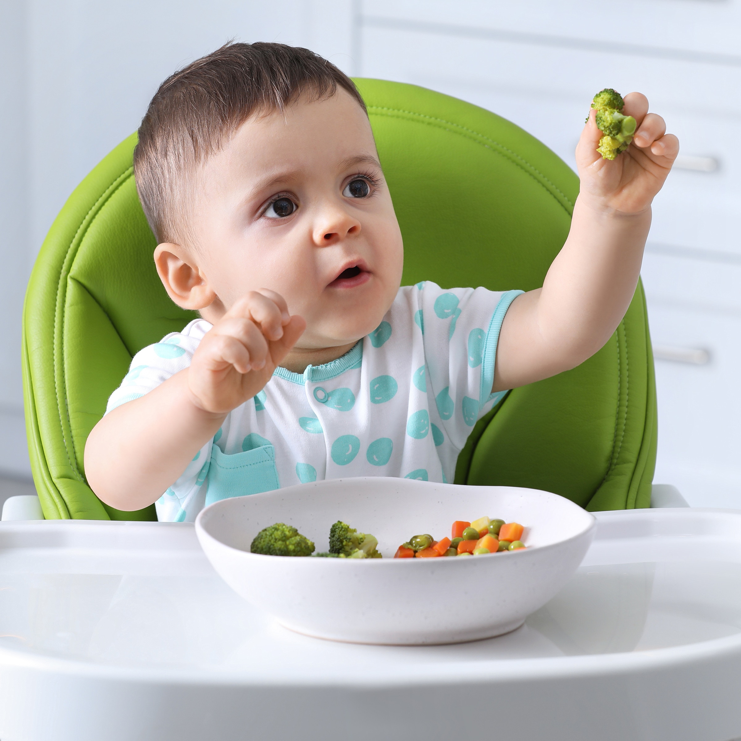 Baby in high chair eating finger-food vegetables, Childbirth Graphics parenting education for optimal infant nutrition