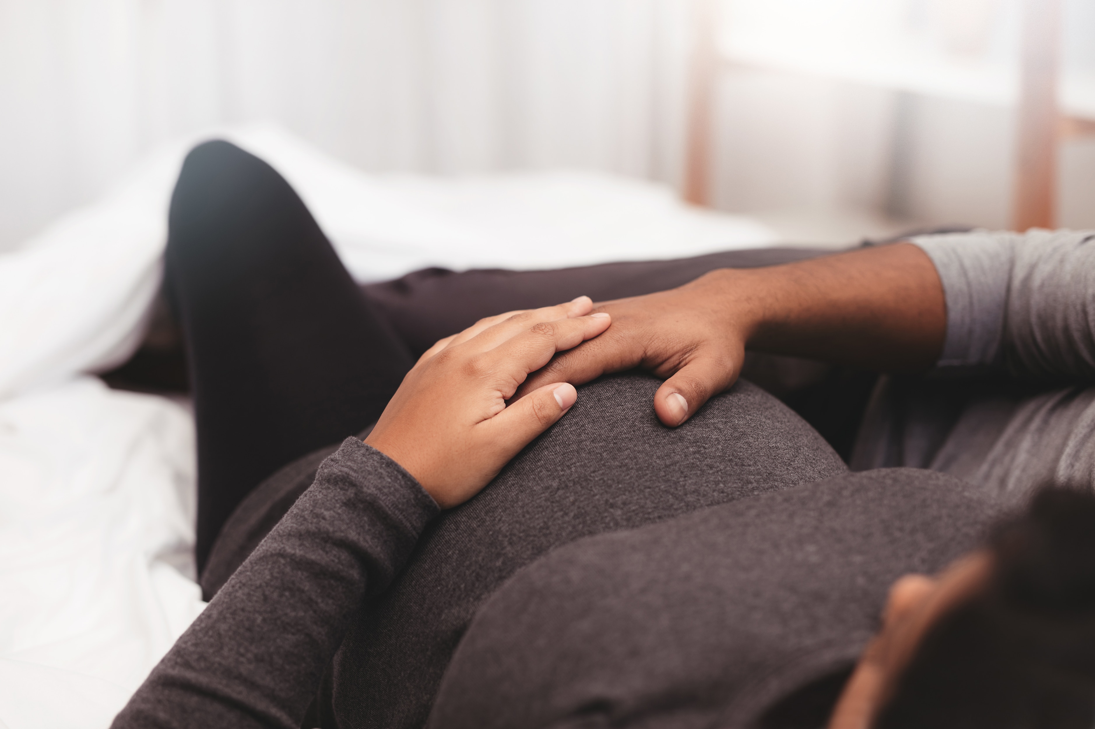 Pregnant couple cuddling on couch with hands on mom’s growing belly