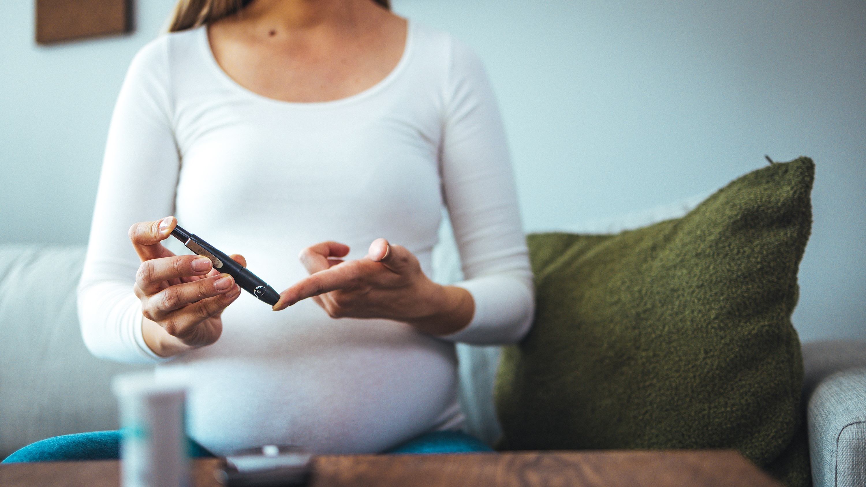 Pregnant woman with gestational diabetes pricking finger to monitor blood glucose levels